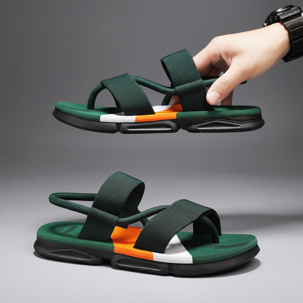 Green and black sandals with orange and white accents held by a hand against a gray background