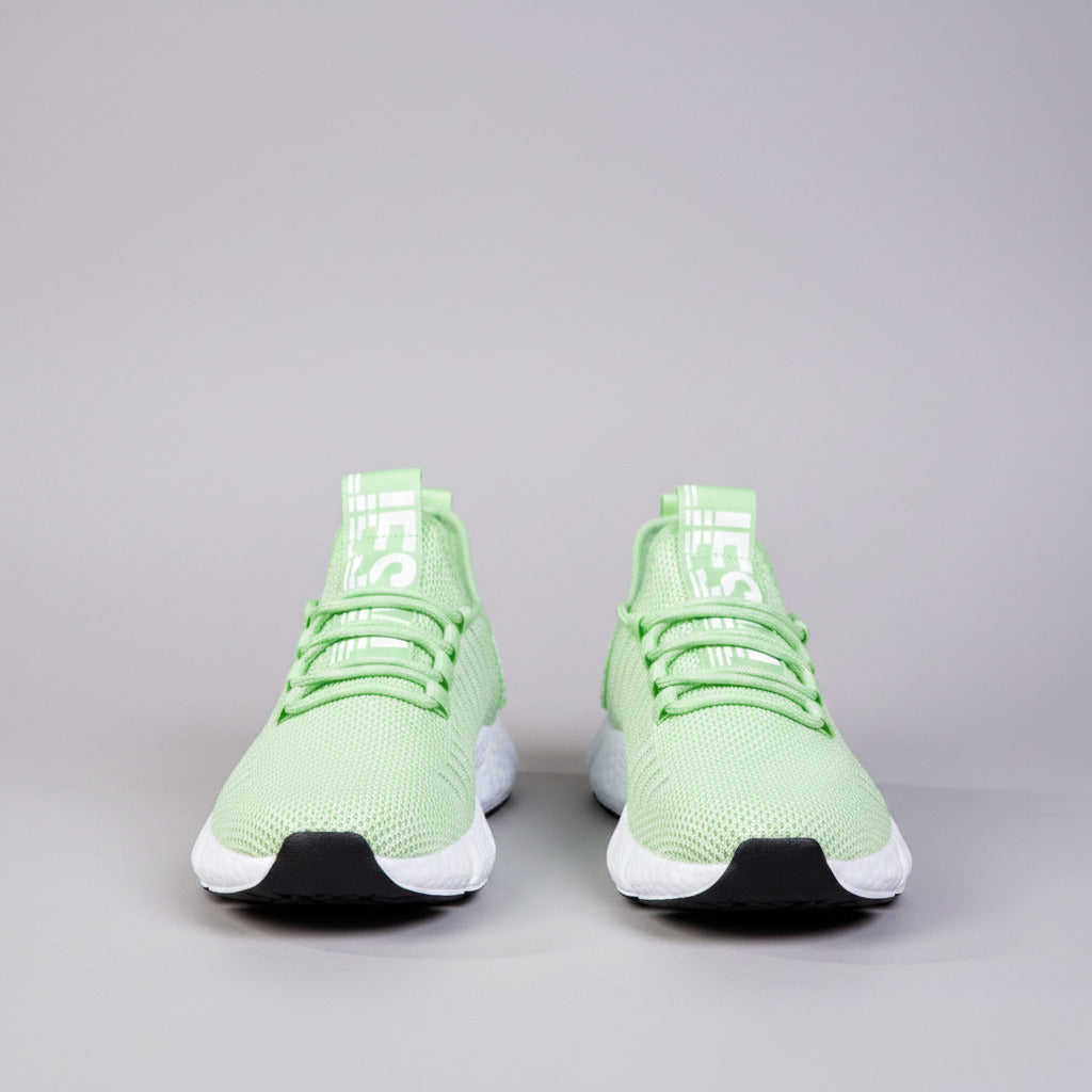 Green athletic shoes with white soles worn by a person on a wooden floor.