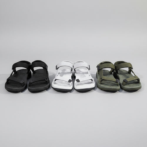 Black, gray, and green sandals displayed on a stone surface with a person wearing black sandals.