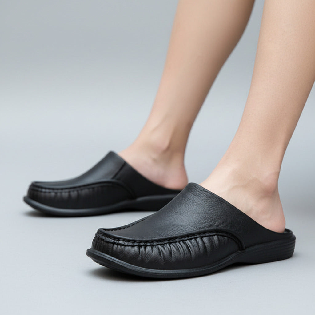 Black slip-on shoes worn by a person on a stone floor.