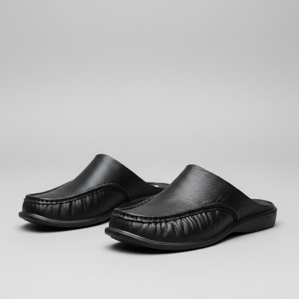 Black slip-on shoes worn by a person on a stone floor.