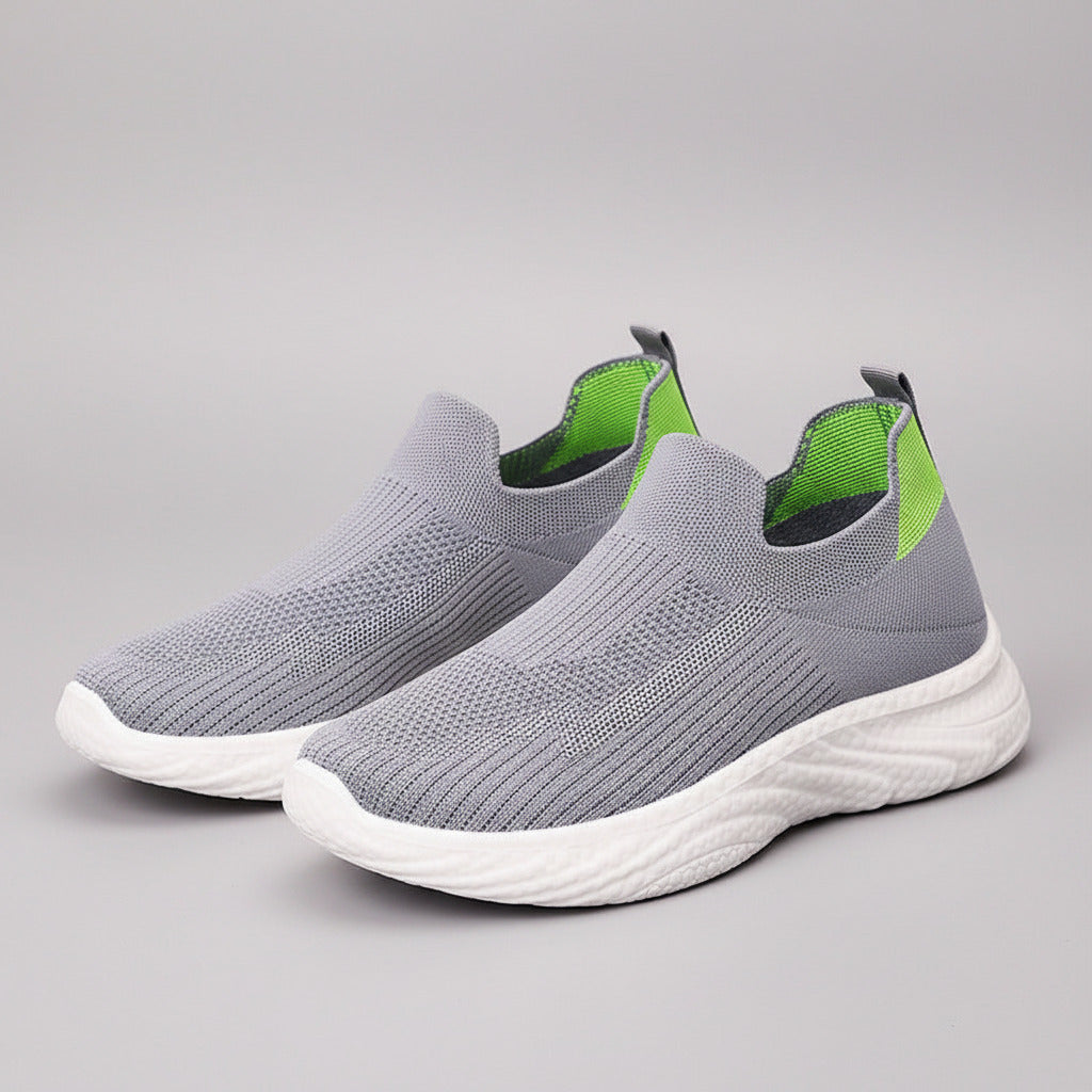 Gray slip-on sneakers with green accents held by a hand against a neutral background